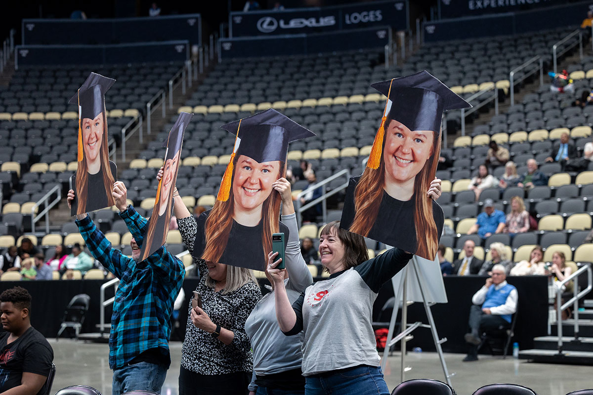 Four people hold large signs featuring a graduate's head