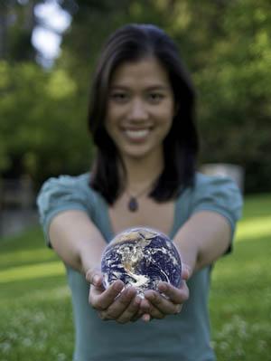 A smiling young woman holds a representation of Planet Earth in her hands.