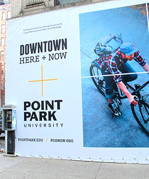 A panel of a colorful banner on the facade of a Point Park University building on Forbes Avenue. The banners promote the city of Pittsburgh's new Downtown retail initiative, which Point Park is supporting.