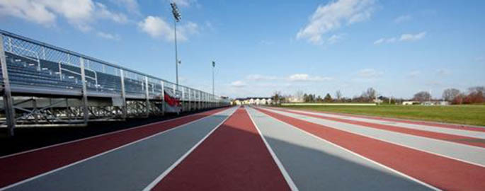 A photo looking down the running lanes at a track and field venue under a sunny blue sky.