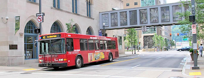 A red Port Authority bus cruises down Wood Street, providing convenient mass transit service to Point Park University in Downtown Pittsburgh.