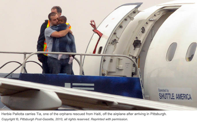 Point Park student Herbie Pallotta carries Tia, a Haitian girl, off the airplane in Pittsburgh. | Co