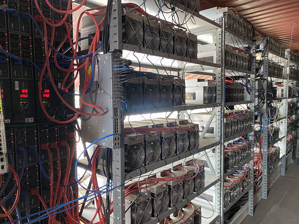 Shelves of Bitcoin miners generate approximately $600,000 in Bitcoin per day at Stronghold Digital Mining's Scrubgrass Power Plant. The miners are cube-shaped machines with built-in fans.