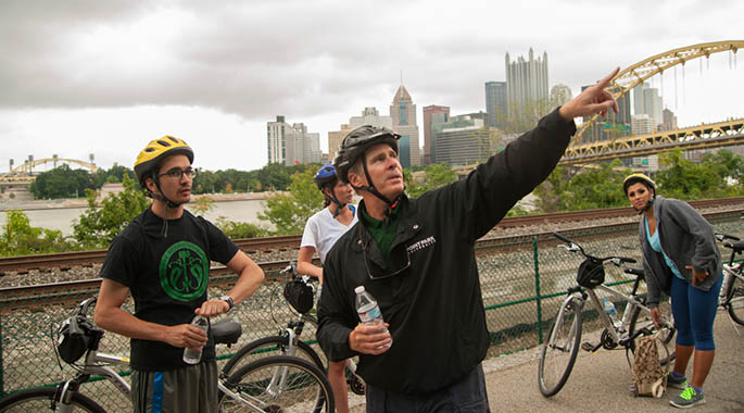 With the Pittsburgh skyline in the background, Point Park President Paul Hennigan points out a feature of the city landscape during a stop on his annual bike ride with a group of Point Park students. | Photo by Christopher Rolinson