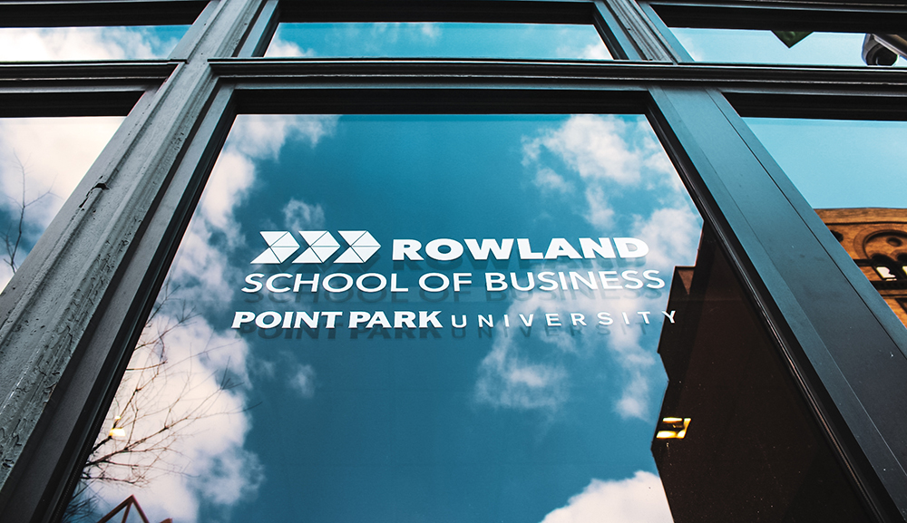 Pictured is the Rowland School of Business logo on a window with clouds reflecting on the glass. Photo by Nathaniel Holzer.