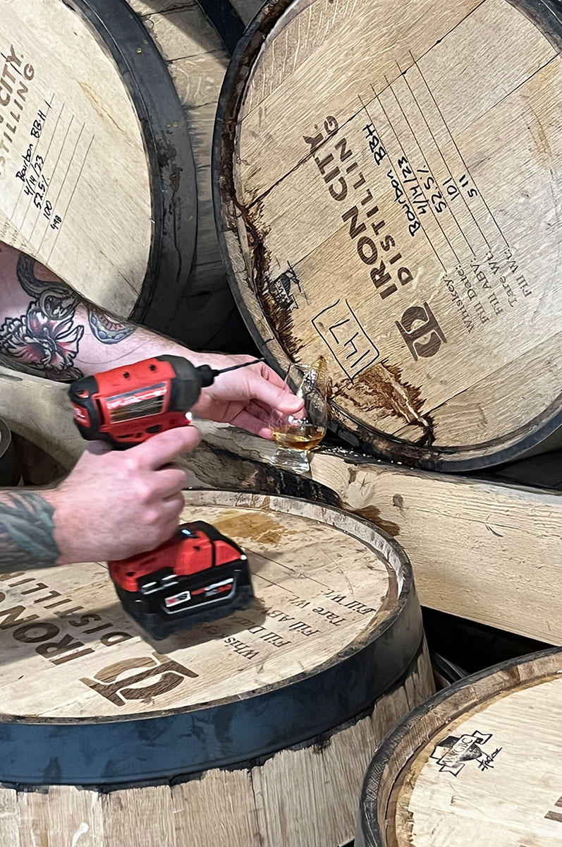 A man drills into a whiskey barrel.