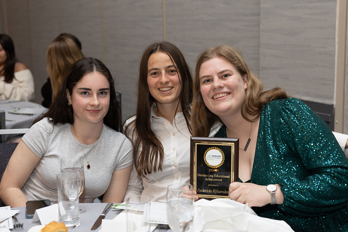 Three students pose at a table, one holding an award.