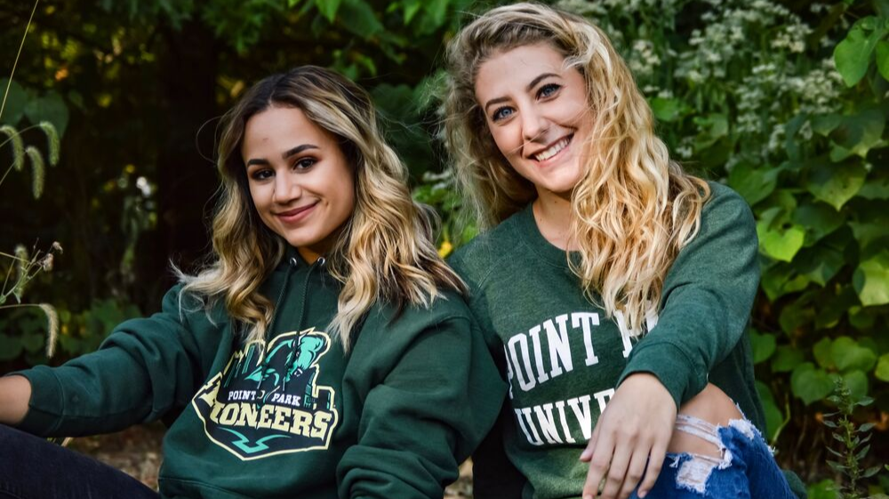 Two students wearing Point Park apparel in front of fall foilage