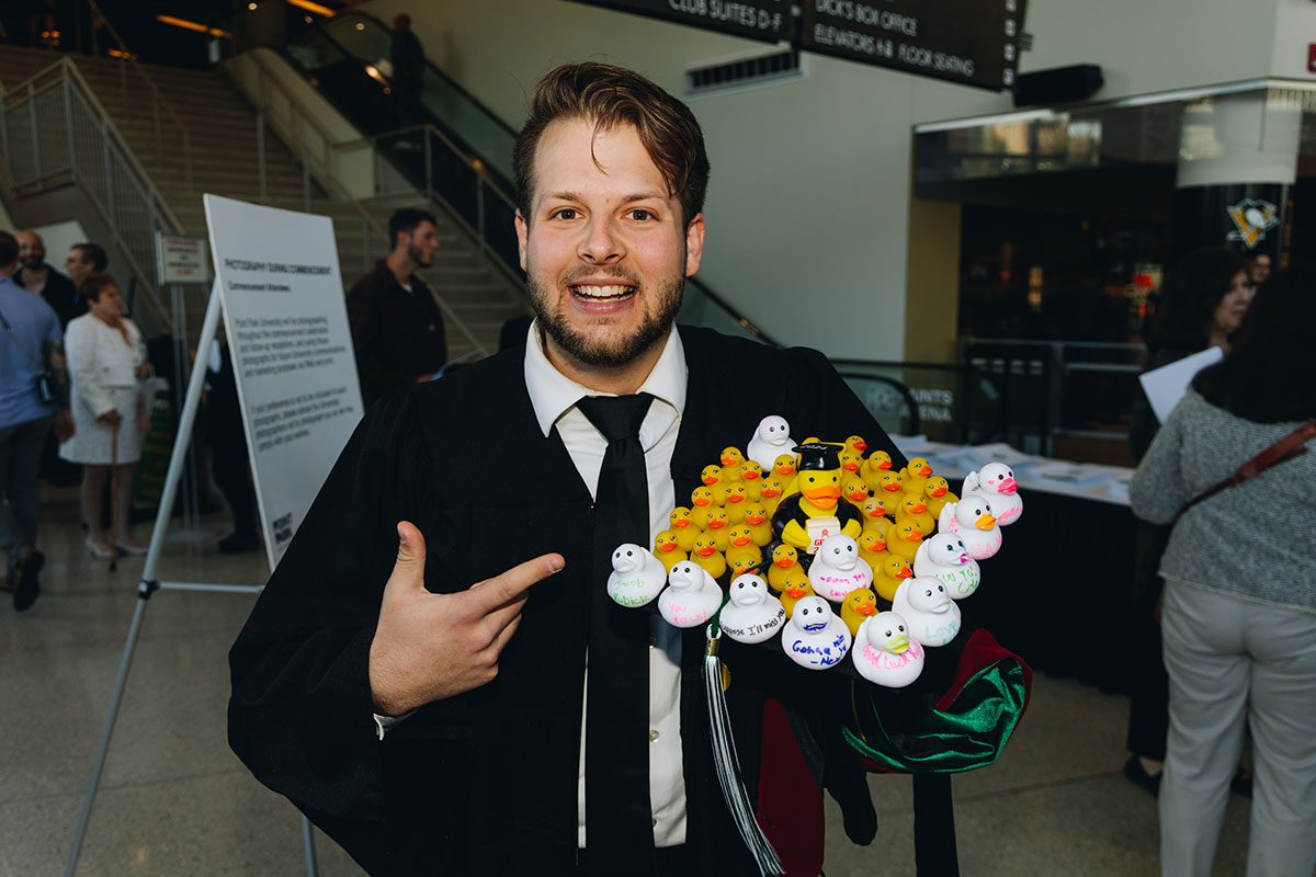 A graduate holds up his cap which is decorated with rubber ducks