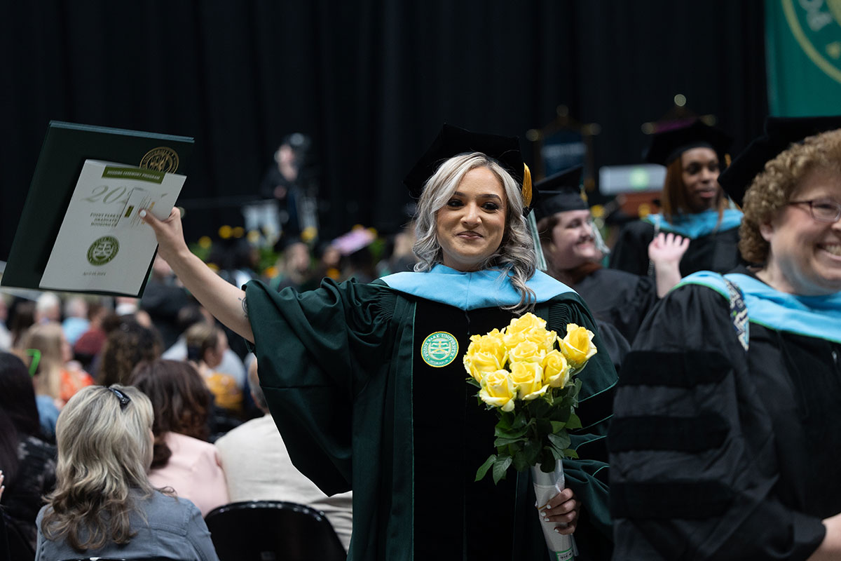 A graduate carries her diploma and a bouquet of roses