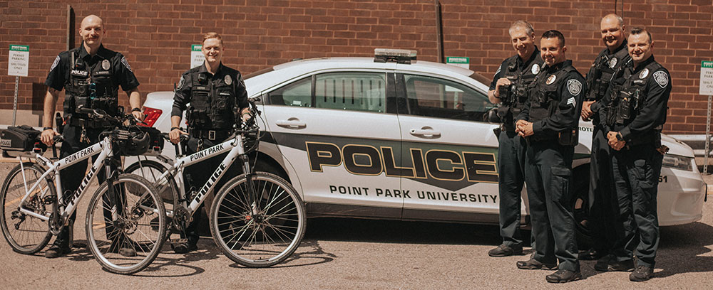 Police officers standing with bikes and a patrol car in the student center parking lot.