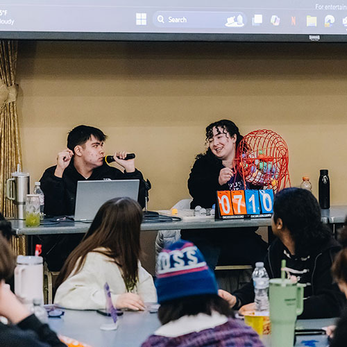 Two students call out Bingo numbers from a table.