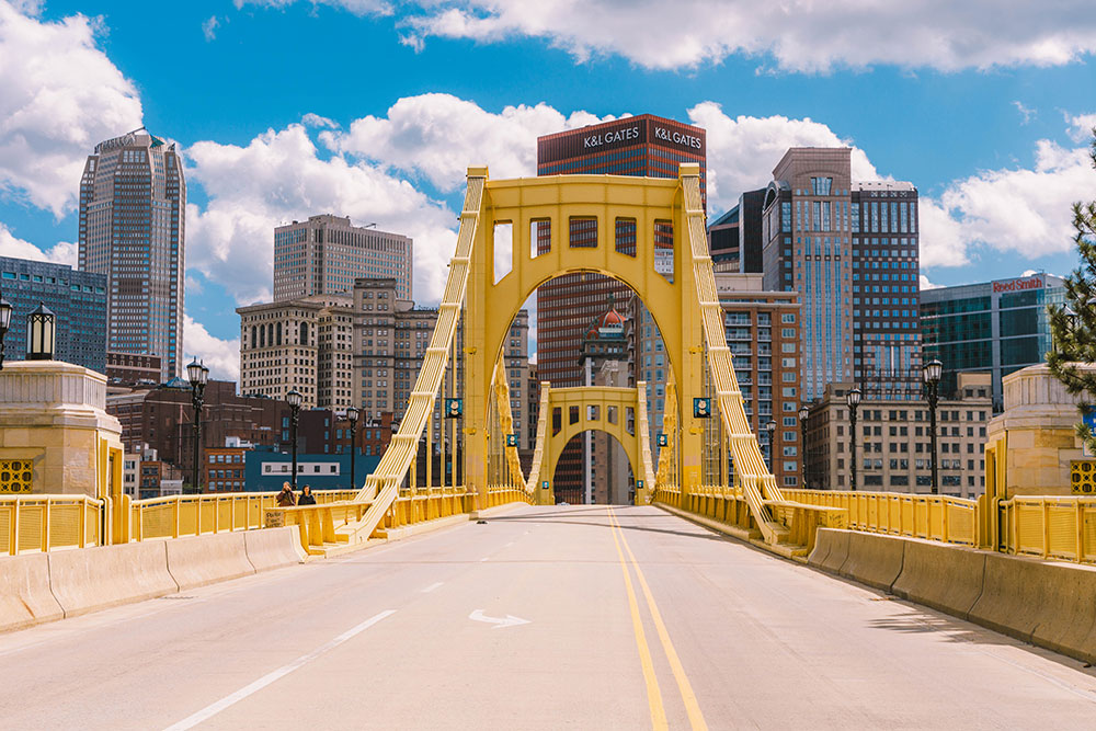 A yellow bridge leads to a city skyline.