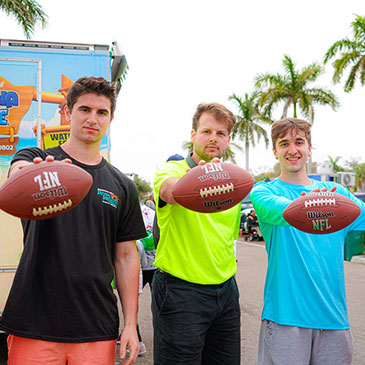 Three young men hold a football in front of them.