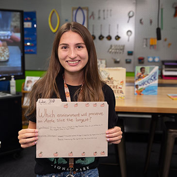 A female student stands in the Matt's Maker Space, holding up a manila folder.
