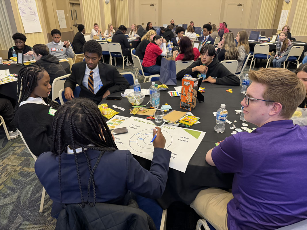 High School students sit at tables filling out a chart. 