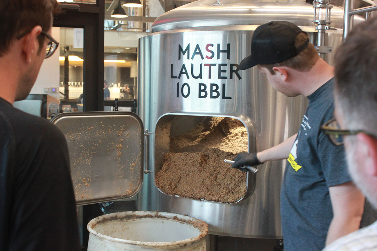 A man moves brown powder from a steel cylinder to a plastic bucket.