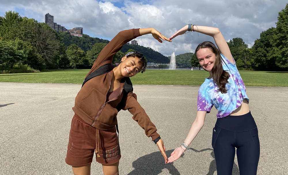 Pictured are two students making a heart shape with their arms in Point State Park during the Fall 2022 Welcome Weekend.