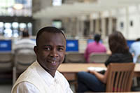 An international student smiles as he sits in Point Park's University Center library as other students work on their studies at tables around him.