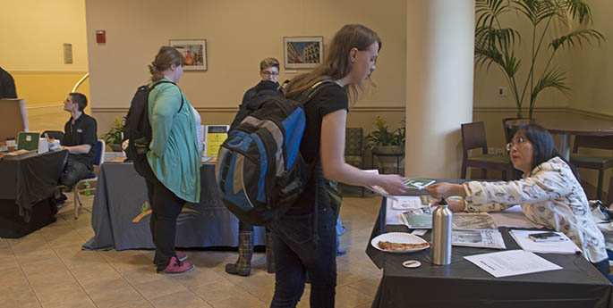 A representative of the Squirrel Hill Coalition hands a neighborhood brochure to a Point Park student during the first-ever City In A Room event to encourage students to explore Pittsburgh. | Photo by Shayna Mendez