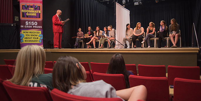 Point Park students sit in folding chairs in the GRW Theatre while playing the Roommate Game, a competition to show how well pairs of roommates really know each other. | Photo by Christopher Squier