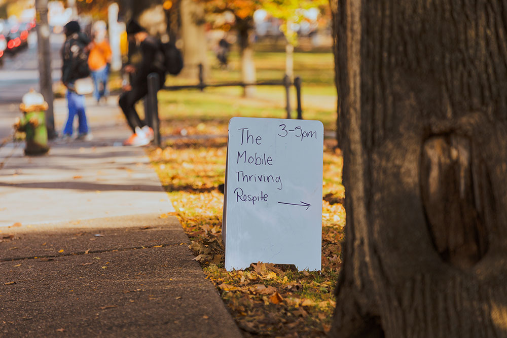 Pictured is a sandwich board sign that states "Mobile Thriving Respite 3-5 p.m." in Allegheny Commons Park. Photo by Ethan Stoner.