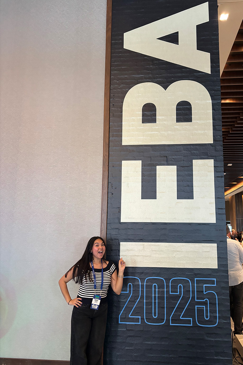 Grace Thomas, a SAEM major expected to graduate in the Spring of 2026, poses in front of a sign at the International Entertainment Buyers Association Conference in 2025.