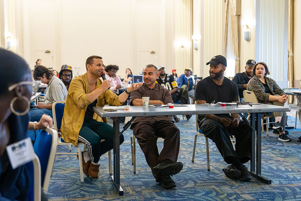 Chris Pandolfi, Yassine Saidi and LaMar Taylor sit at a table critiquing a student's pitch.