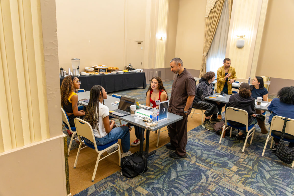 Yassine Saidi stands and talks to students at a table.