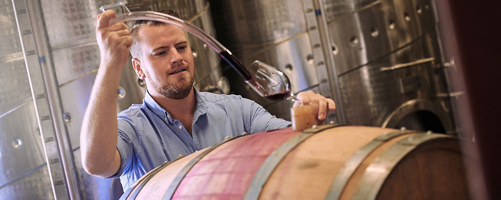 A man funnels wine from a barrel into a glass.
