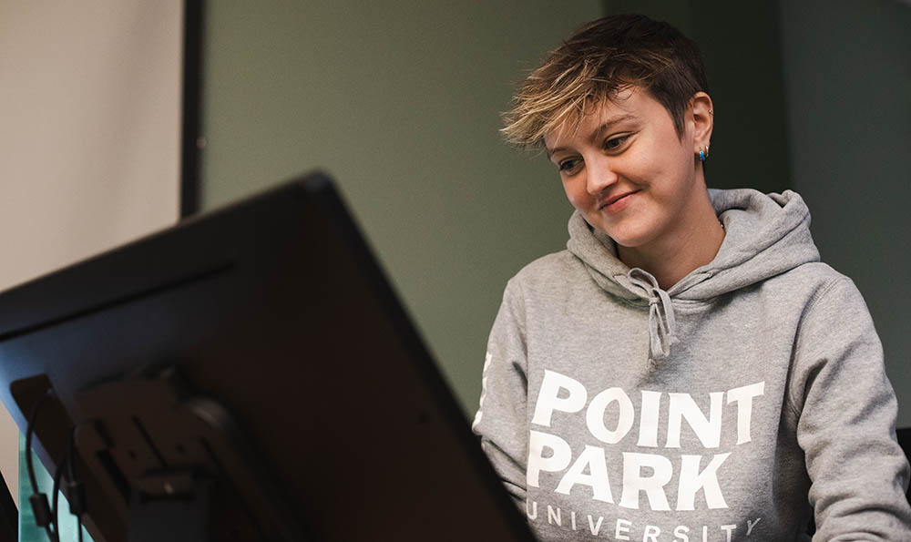 A student using a computer wears a Point Park sweatshirt. Paskill image restricted use until August 2028. 