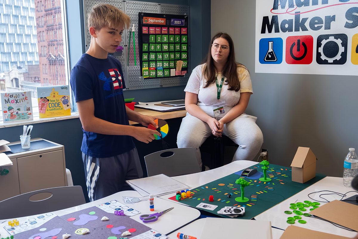 A student describes his board game while another listens.