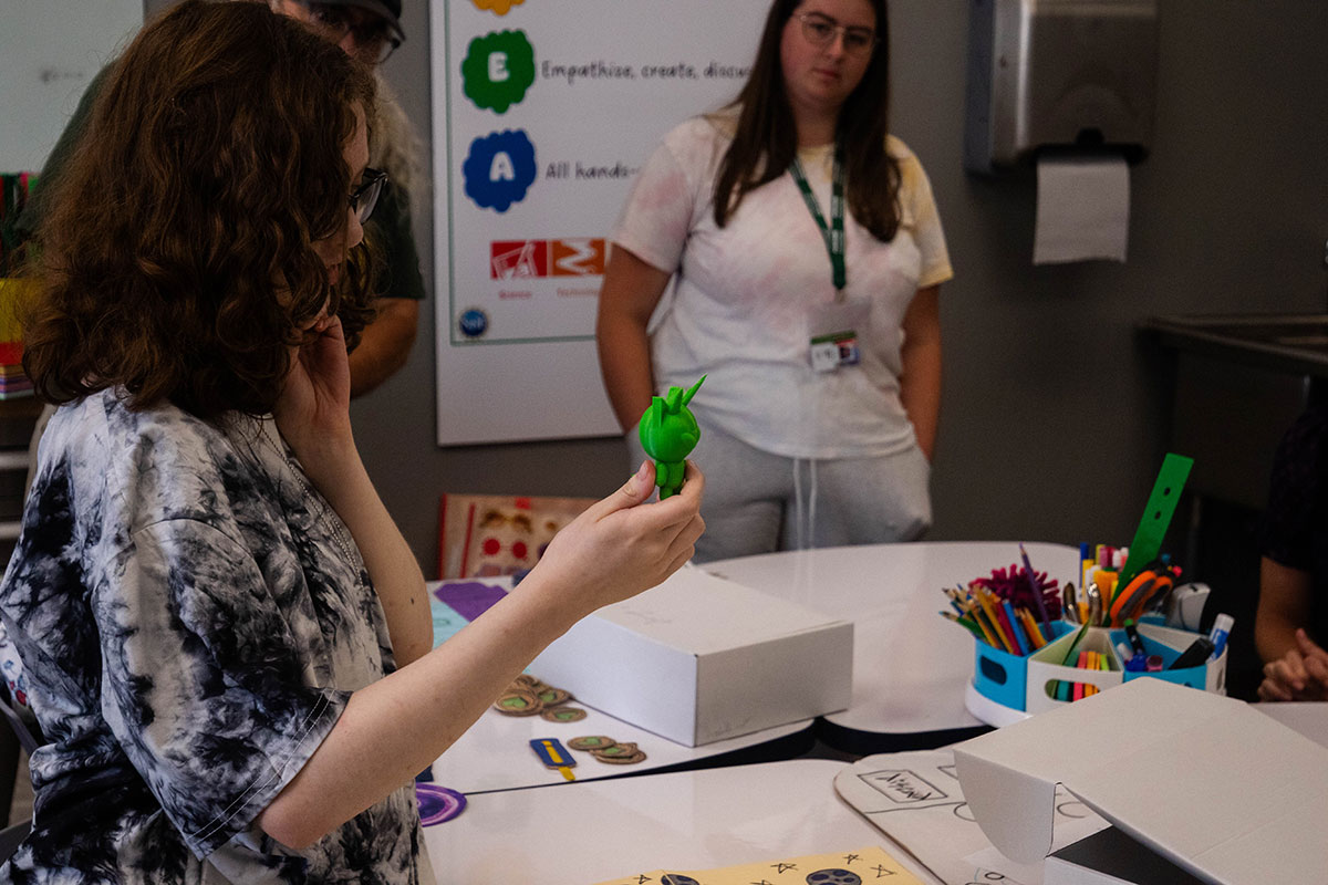 A student holds up a 3-D printed character while others listen.