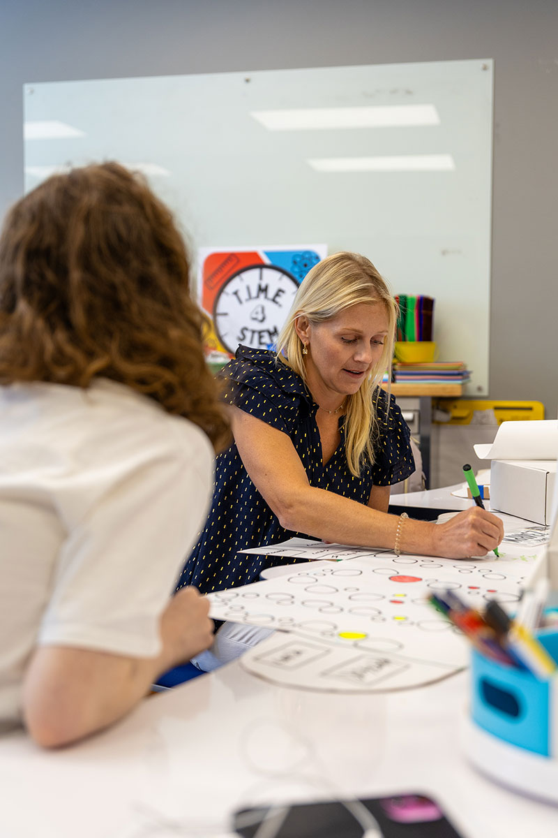 A teacher discusses a students idea at a table.