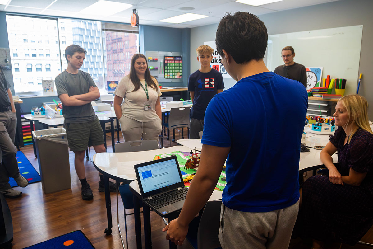 A student presents his board game while others listen. 