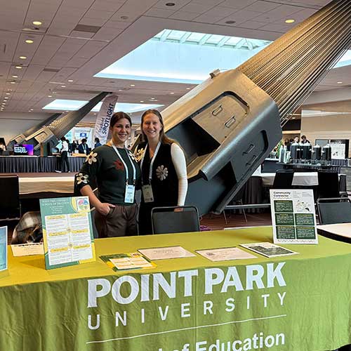 Two students stand behind a table with a Point Park tablecloth.