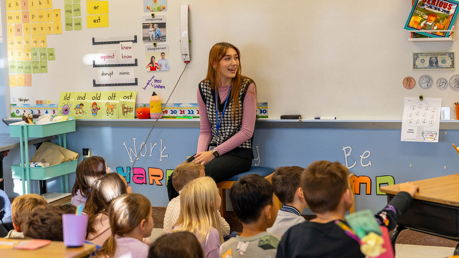 A student teacher sits in front of a classroom with children looking at her.