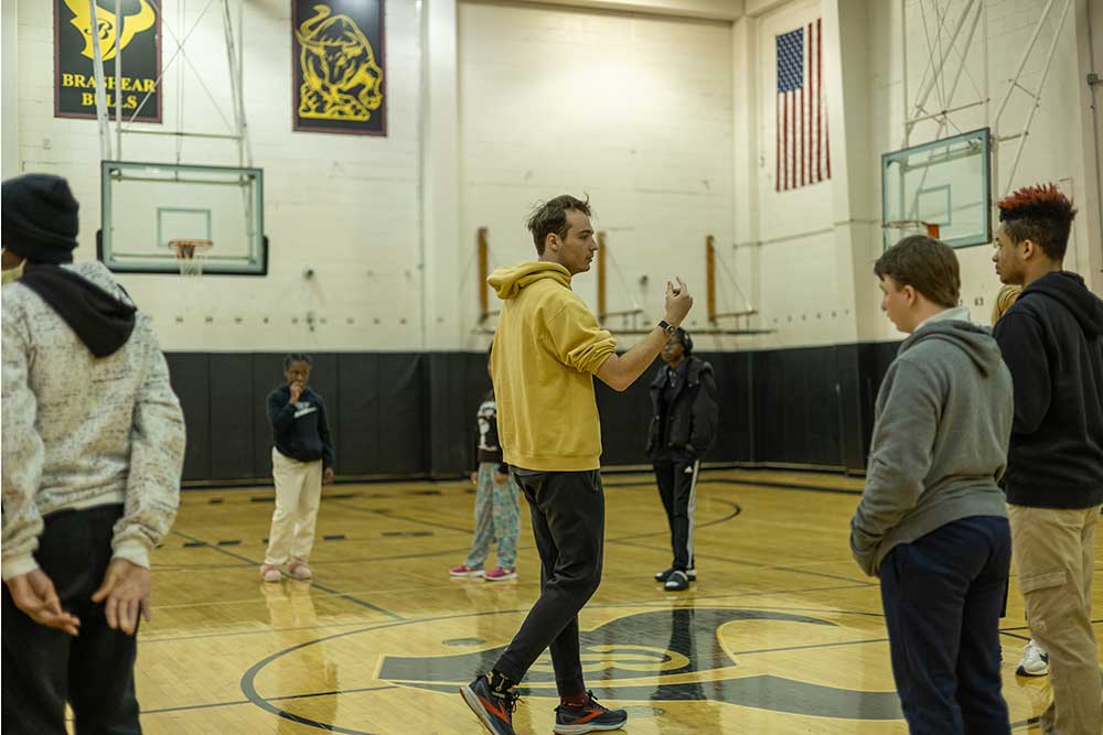 A Point Park student walks in a gym surrounded by high school students.