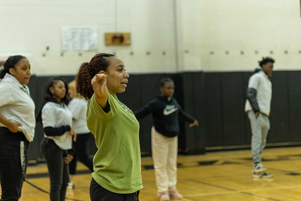 A Point Park student points and gives directions in a gym of high school students.