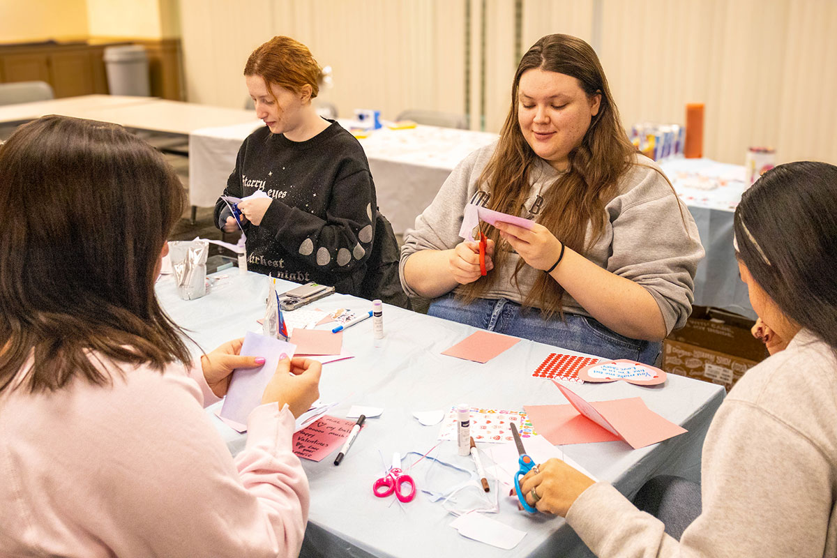 Students sit around a table and decorate cards.