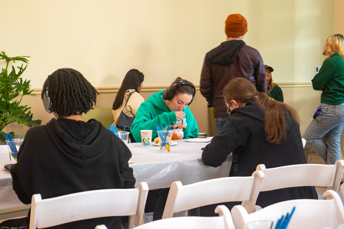 People paint pumpkins at a table.