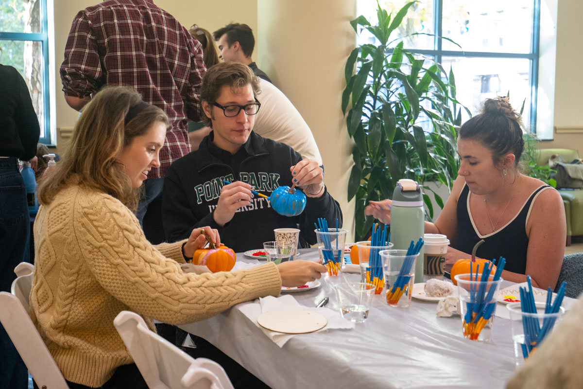 People paint pumpkins at a table.