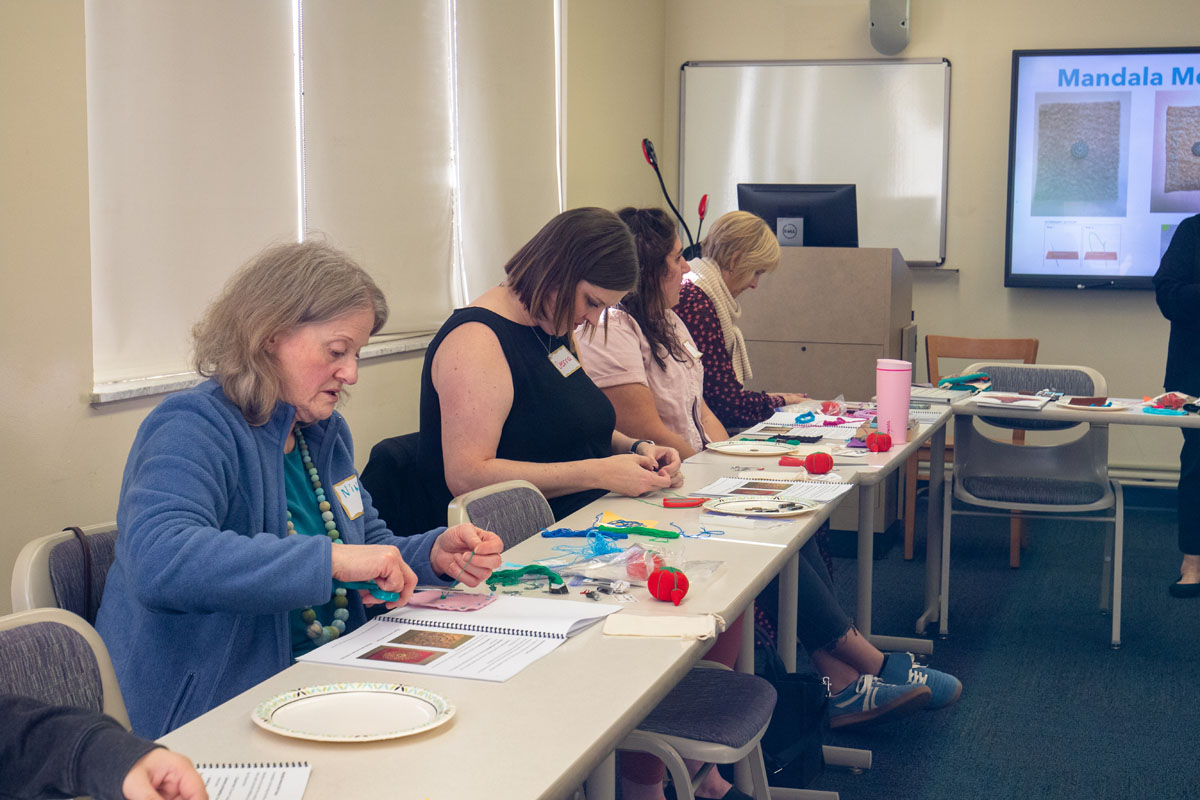 People sit a table doing embroidery.