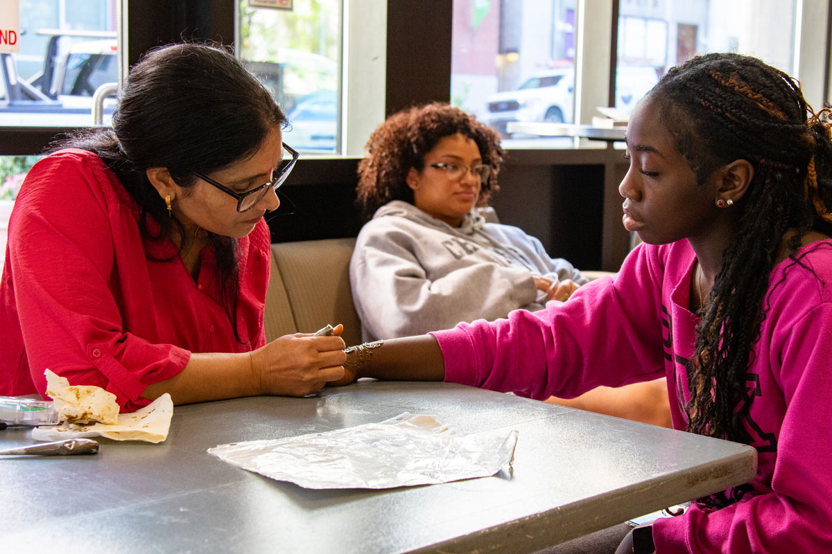 A woman draws a henna tattoo on a student's hand.