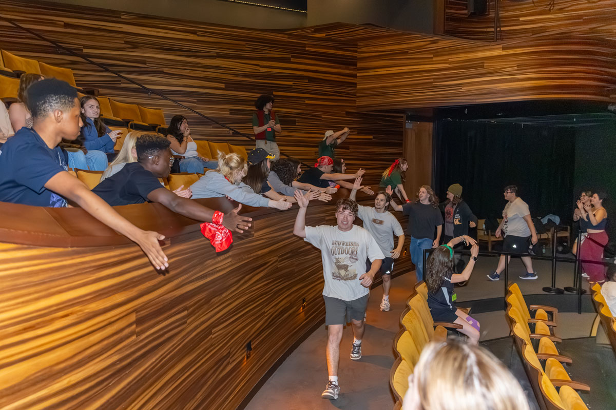 Students walk into PNC Theatre slapping hands with people they pass. 
