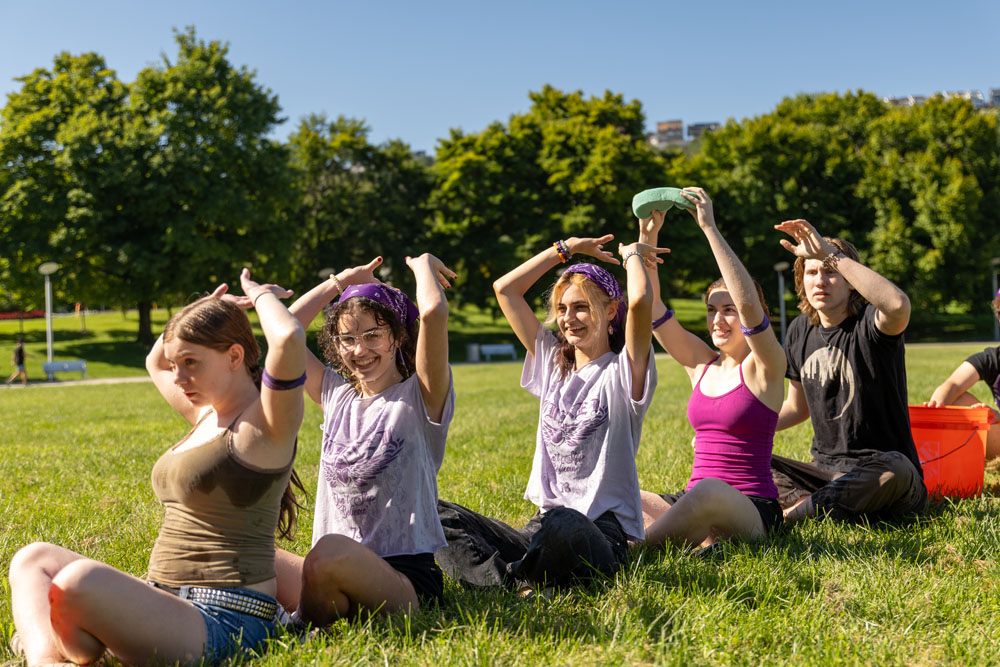 Students sitting cross-legged in a park pass a sponge over their heads.