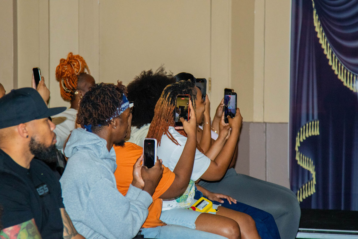 Audience members hold up their phones to photograph the person on the catwalk.