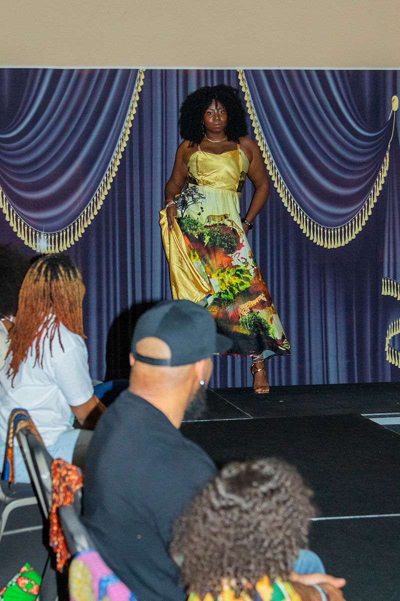 A woman on the catwalk wears a colorful long dress.