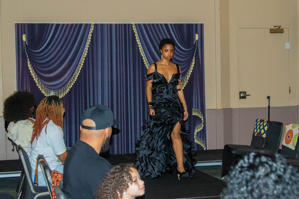 A woman walks on the catwalk wearing a long black dress.