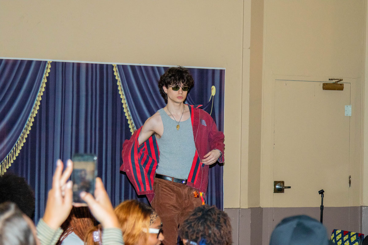 A man walks on the catwalk as he pulls on a red button-down shirt.
